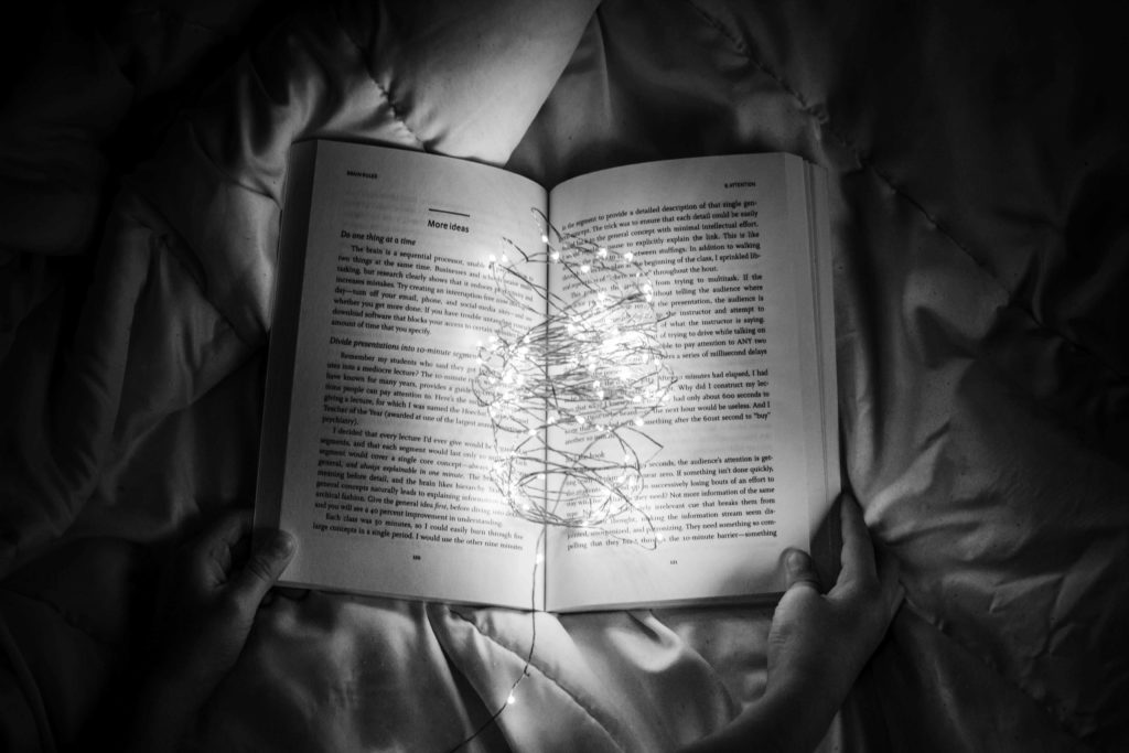 black and white image of a book held by two hands open in the middle with string lights