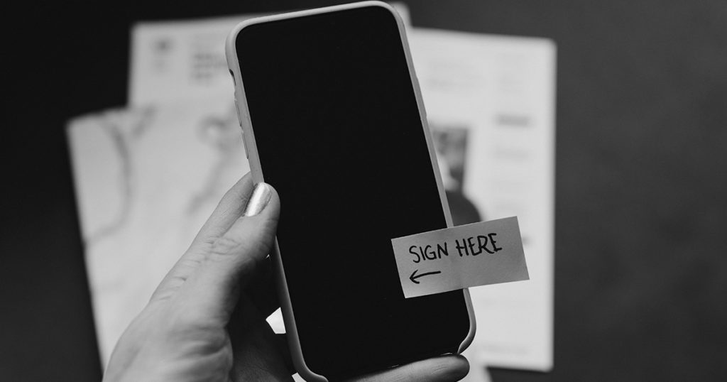 Black and white image of mobile phone with a sticker that says 'sign here' on it.