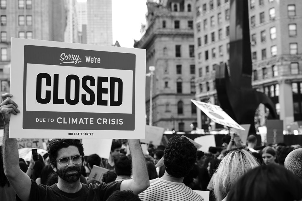 black and white image of a climate march with a person holding up a sign saying "sorry, we're closed due to climate crisis."