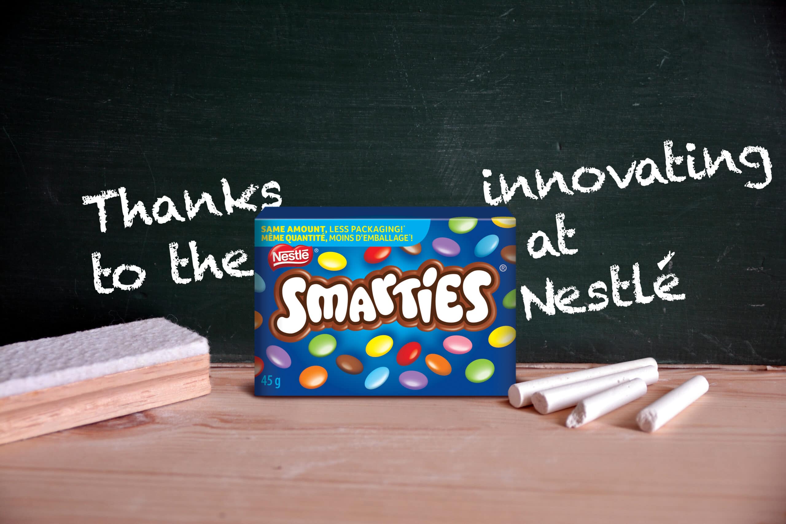 A Smarties box on the table with floating text that connects to the brand logo name which reads, "Thanks to the SMARTIES innovating at Nestlé"