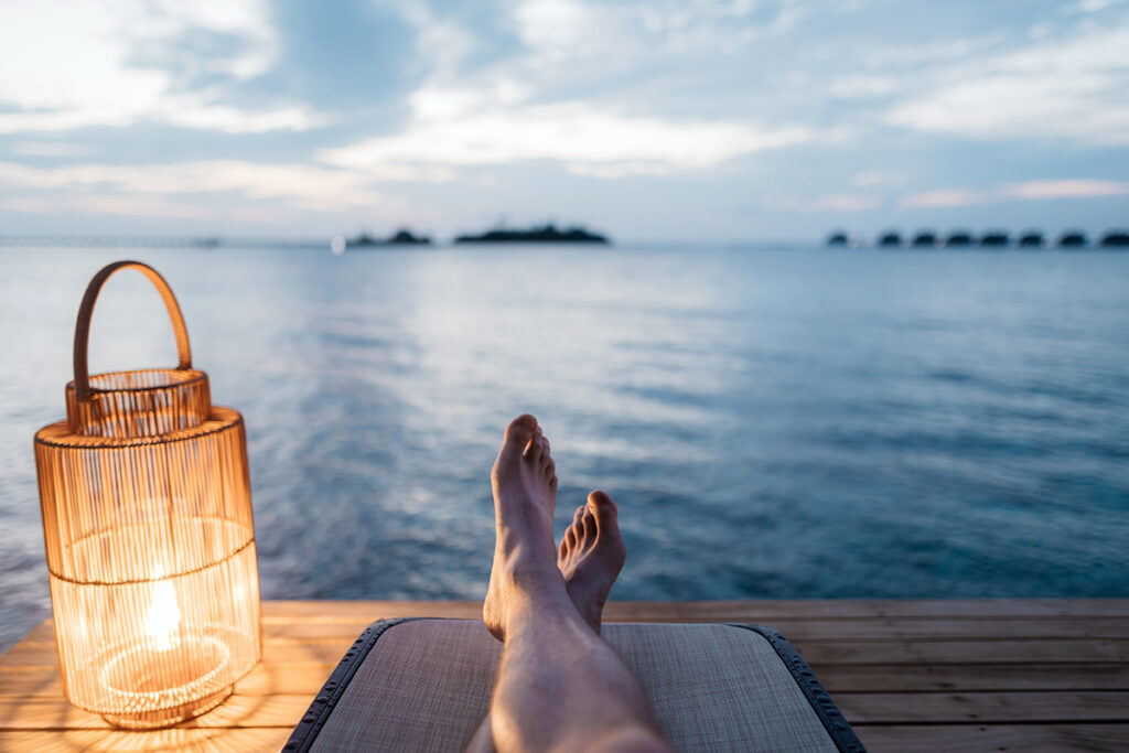 Feet relaxing on a dock in front of a lake with a lantern by the side