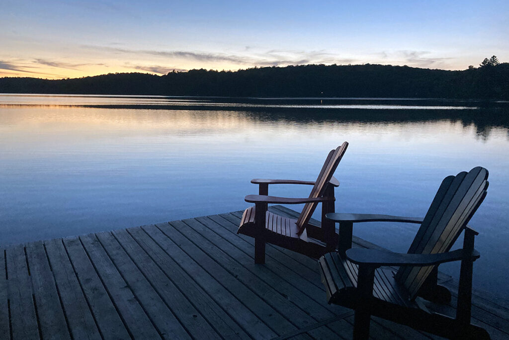 Muskoka chairs on a dock in front of a lake