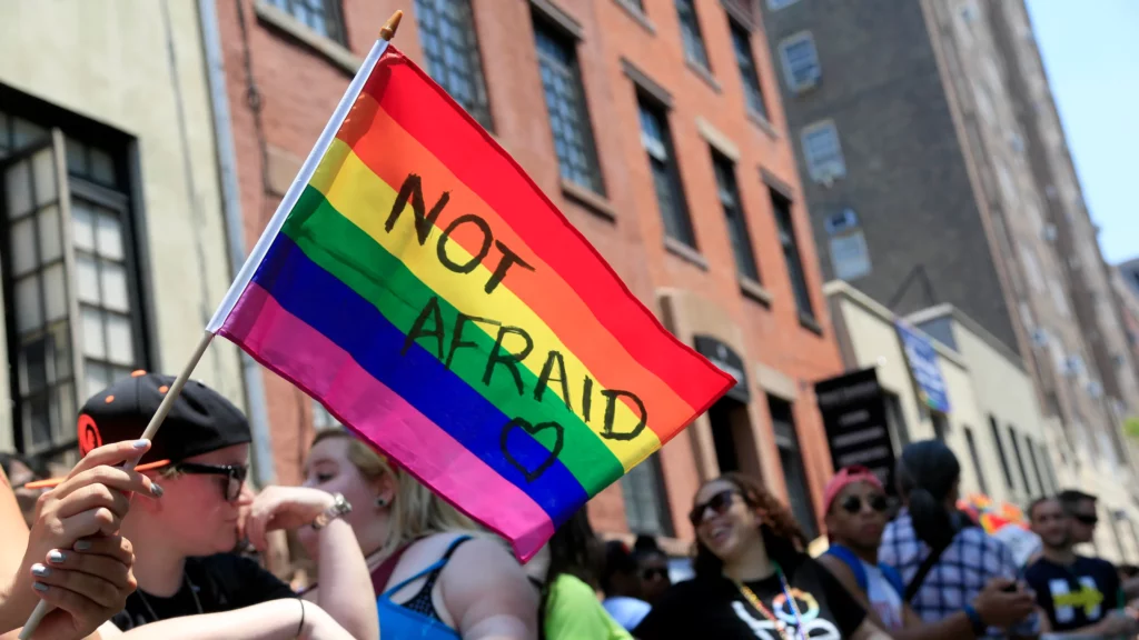 Pride flag being held at a parade, with the words 'Not Afraid" written across it.